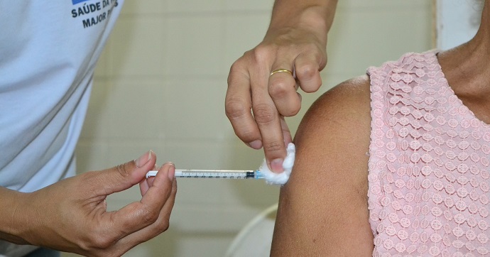 Close-up de profissional de saúde aplicando a vacina da gripe no braço de um paciente em posto de saúde de Montes Claros.