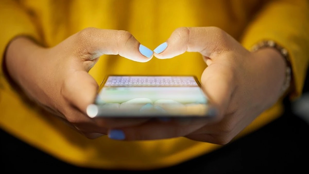 Pessoas segurando um smartphone com as mãos e digitando na tela sobre fundo amarelo vibrante.