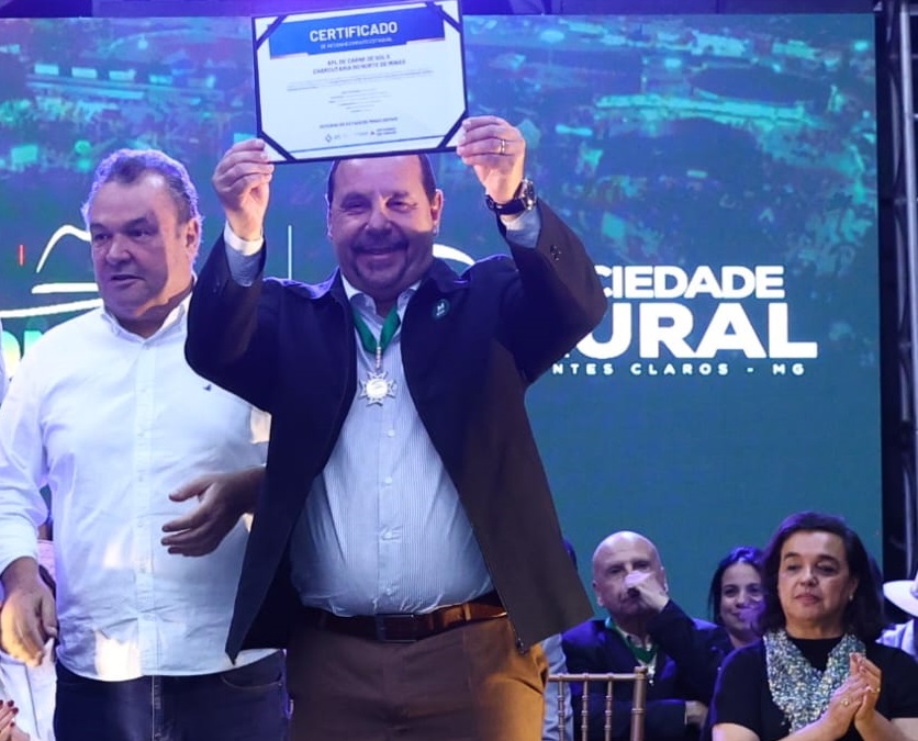O prefeito de Montes Claros, Guilherme Guimarães, em pé no palco da Expomontes 2026, segurando sorridente e erguendo o certificado de reconhecimento do APL da Carne de Sol e Charcutaria do Norte de Minas.