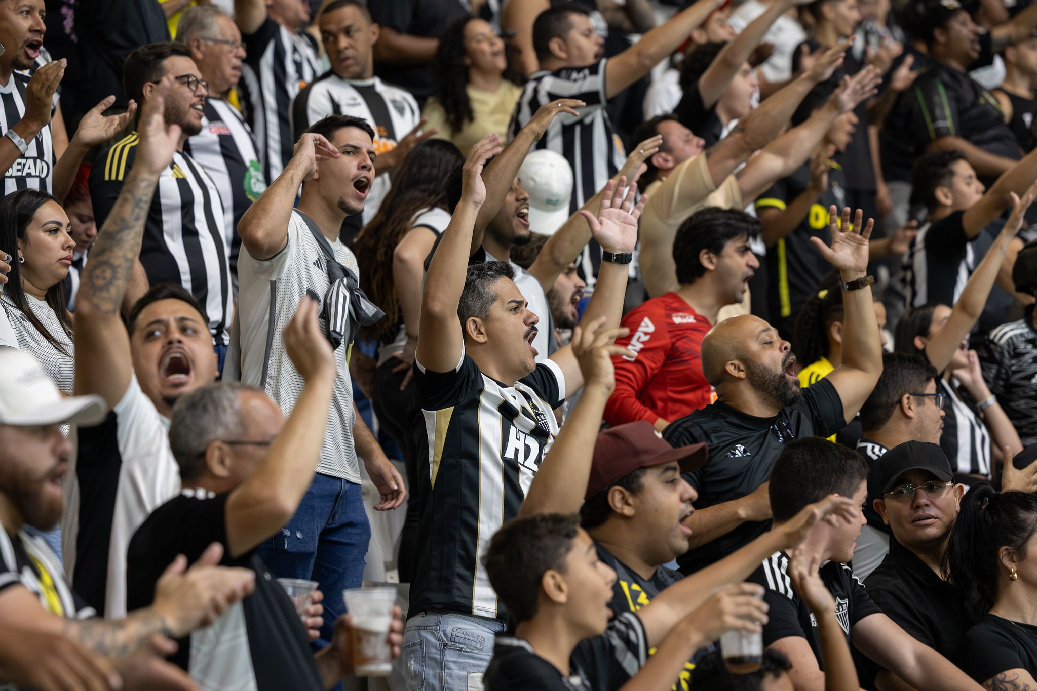 Torcedores do Atlético Mineiro com camisas alvinegras cantando e vibrando na arquibancada da Arena MRV.