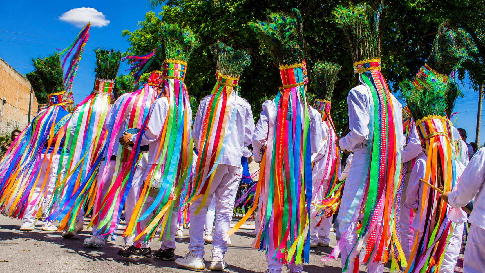 Integrantes de ternos de catopês com trajes brancos e fitas coloridas tocando tamborins durante cortejo festivo no centro de Montes Claros.